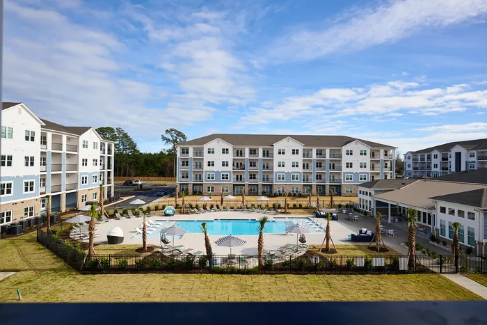 Aerial view of a modern apartment complex with a pristine pool area surrounded by lush landscaping.