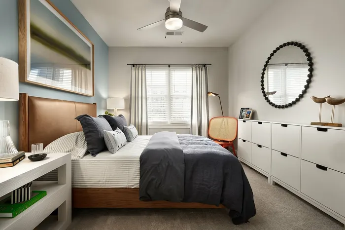 Cozy bedroom with stylish decor, featuring a plush bed, artistic wall decor, and ample natural light.