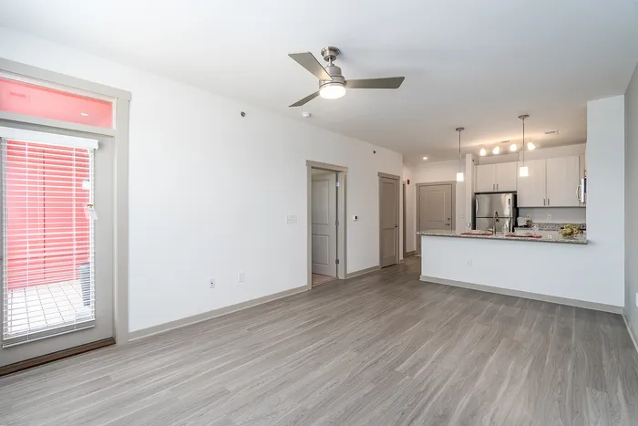 Bright and modern apartment with open-plan kitchen, sleek ceiling fan, and elegant light-colored flooring.