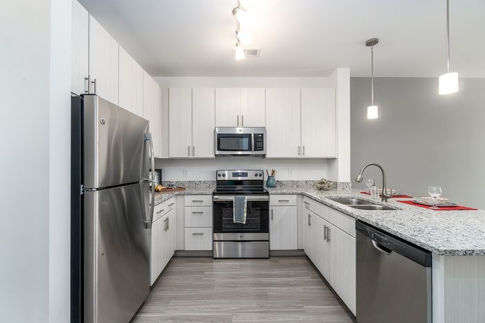 Modern kitchen with sleek stainless steel appliances, elegant white cabinetry, and a chic granite countertop, illuminated by stylish pendant lighting.