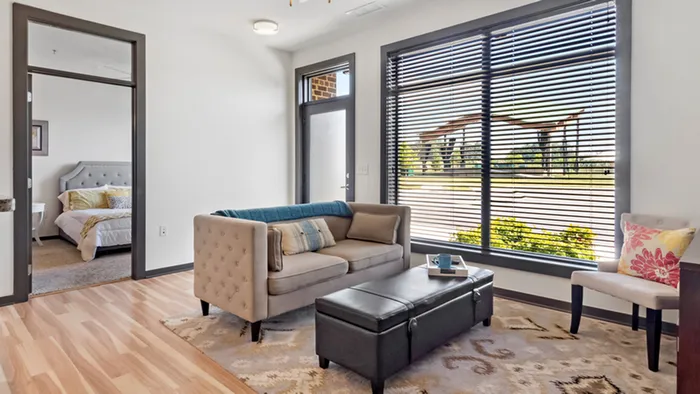 Bright and inviting living room with modern sofa, expansive window views, and cozy adjoining bedroom, perfect for relaxation.