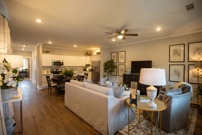 Elegant open-concept living room with cozy seating, chic decor, and a modern kitchen in the background, featuring warm lighting and stylish wooden flooring.