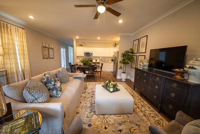 Elegant living room with cozy seating, decorative pillows, and vibrant greenery next to an open-concept kitchen.