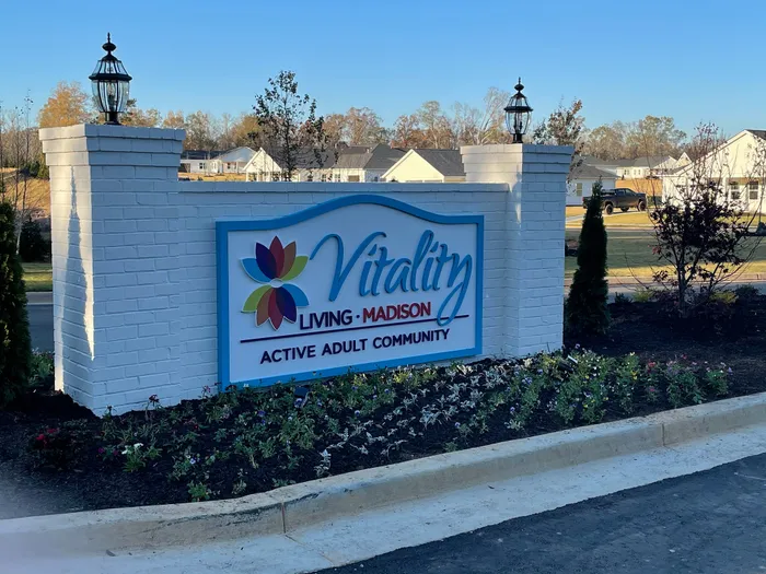 Charming entrance sign for Vitality Living Madison, an active adult community, surrounded by lush greenery and elegant lanterns.
