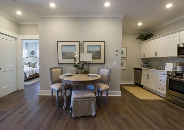 Elegant open-concept apartment featuring a cozy dining area with classic furniture, adjacent to a modern kitchen with sleek white cabinetry and stainless steel appliances.
