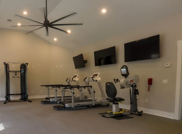 Modern fitness center with state-of-the-art treadmills, workout equipment, and flat-screen TVs under a sleek ceiling fan.