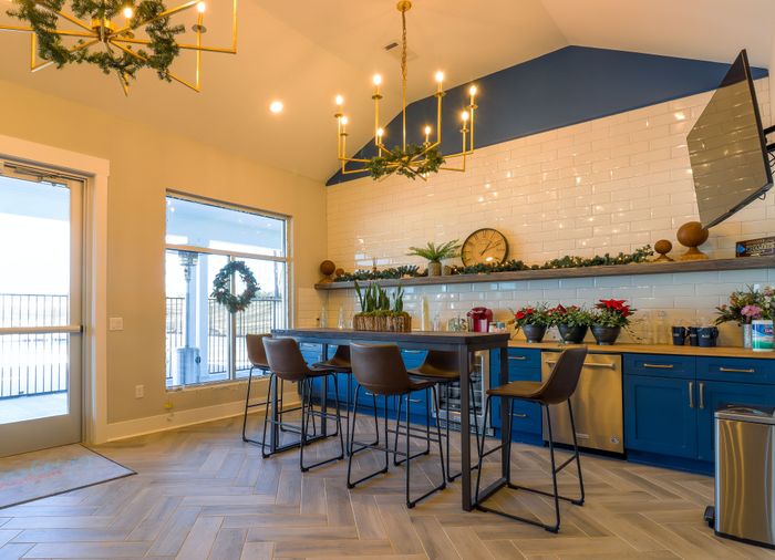 Chic kitchen with blue cabinets, elegant lighting fixtures, and a cozy breakfast bar, enhanced by holiday decor and natural light.