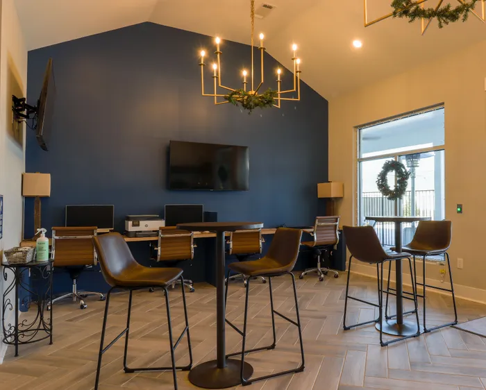 Modern community workspace with sleek decor, blue accent wall, computer stations, and stylish seating under a chic chandelier.