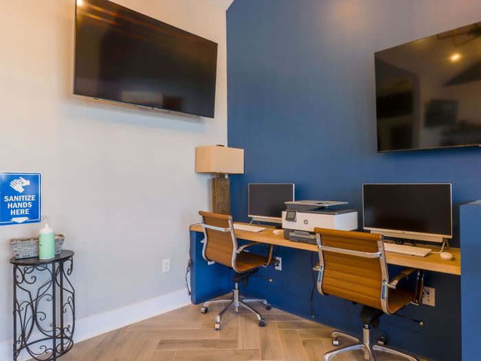 Modern communal workspace featuring sleek computers, a printer, and comfortable leather chairs, perfect for productivity.