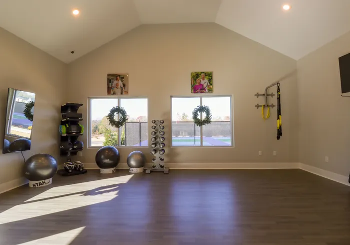 Modern fitness room with large windows, exercise equipment, and a stylish wooden floor.