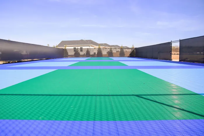 Vibrant pickleball court with colorful playing surface, surrounded by a modern housing community under a clear blue sky.