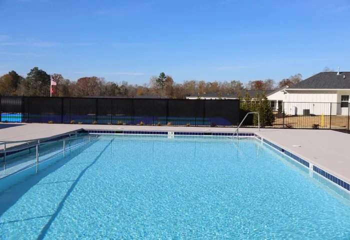 Inviting outdoor pool with crystal-clear water, surrounded by a well-maintained patio and scenic views of trees and residential buildings.