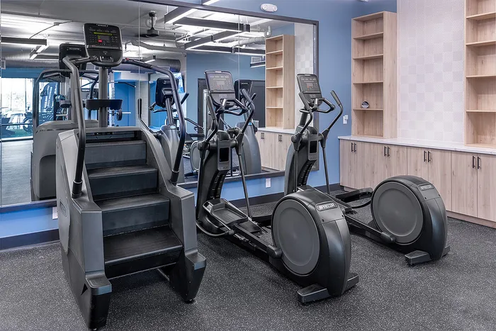 Modern fitness center with state-of-the-art equipment, featuring sleek treadmills and stair climber against a stylish mirrored wall.