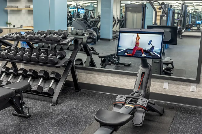State-of-the-art gym with sleek exercise equipment, modern dumbbell rack, and interactive workout screen for a dynamic fitness experience.