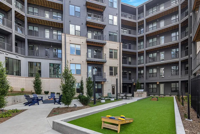 Modern apartment complex courtyard featuring lush green space, cozy seating area, and recreational game setup.