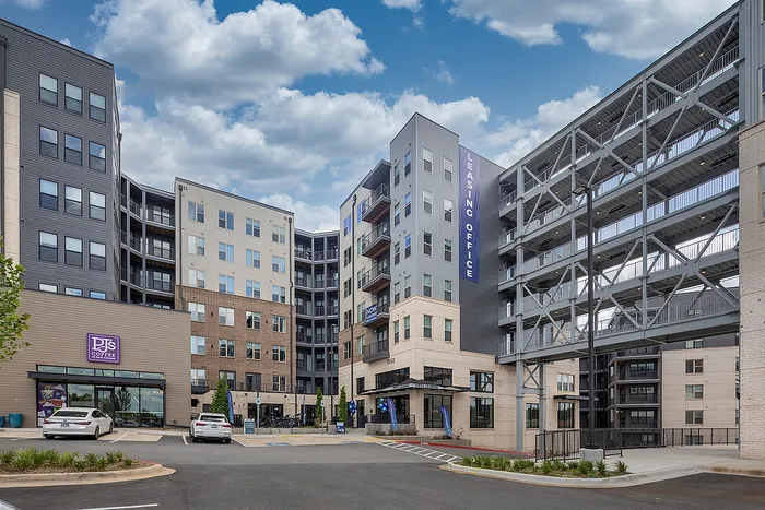 Modern apartment complex with a vibrant leasing office, ample parking, and a cozy coffee shop under a blue sky.