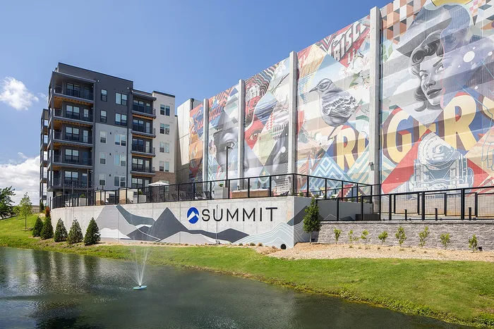 Vibrant apartment complex with eye-catching mural artwork, featuring modern architecture and serene pond setting, perfect for urban living.