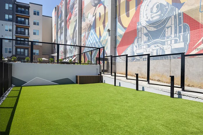 Vibrant urban courtyard with lush artificial grass, captivating mural backdrop, and modern apartment views.