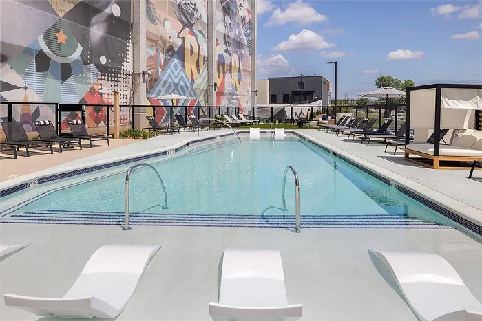 Inviting outdoor swimming pool area with modern lounge chairs, vibrant mural backdrop, and a clear blue sky.