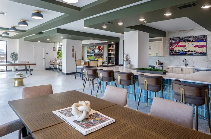 Contemporary open-concept living and dining area featuring modern furniture, a stylish bar with elegant seating, and a large television playing sports.