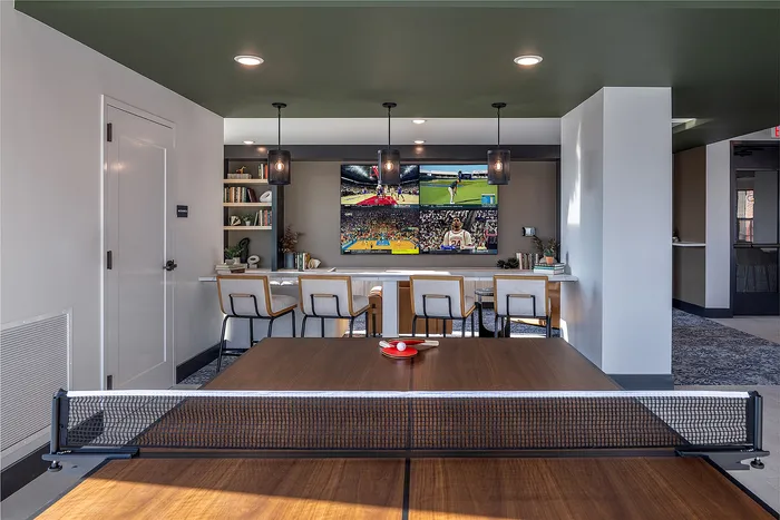Modern entertainment room with a stylish ping pong table, sleek bar seating, and multiple sports screens for a dynamic experience.