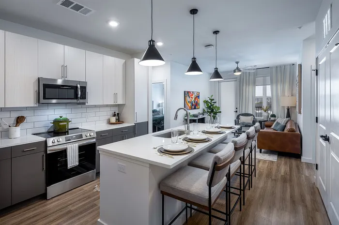 Modern kitchen and cozy living room with sleek appliances, elegant pendant lighting, and stylish bar seating in a chic apartment.