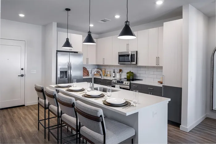 Modern kitchen with sleek white cabinets, stainless steel appliances, and elegant pendant lighting over a spacious island with seating.