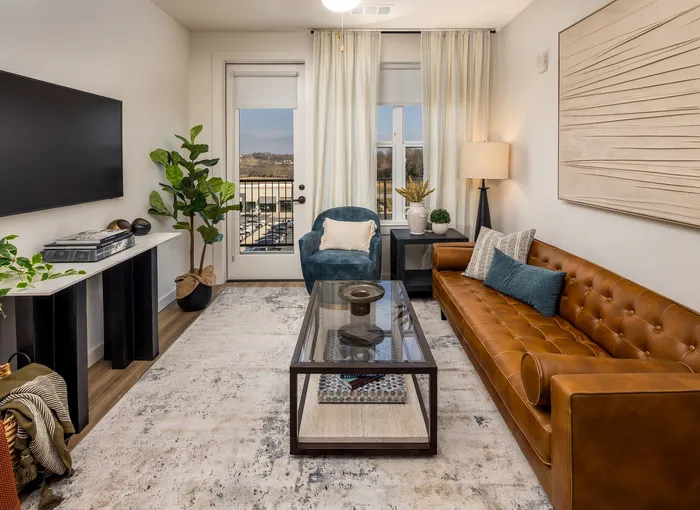 Inviting living room with chic leather sofa, modern glass coffee table, and large TV, complemented by stylish decor and natural light.