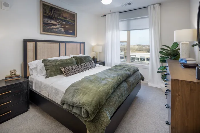 Elegant bedroom with large window, cozy green bedding, and modern wooden furniture, creating a serene and inviting atmosphere.