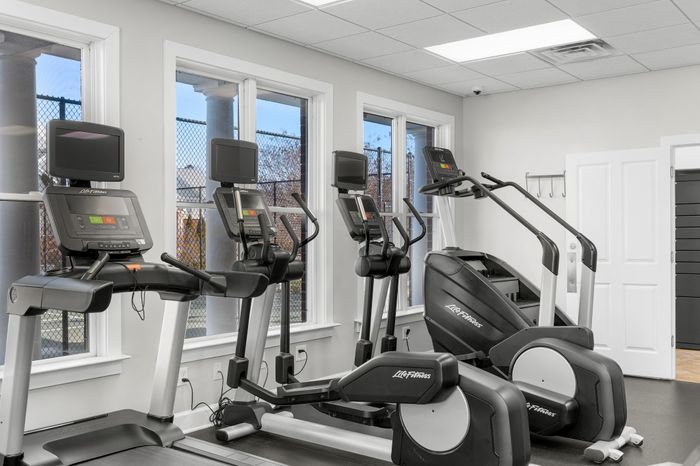Modern fitness center with state-of-the-art Life Fitness equipment, featuring two treadmills and an elliptical, set against a bright, spacious environment with large windows.