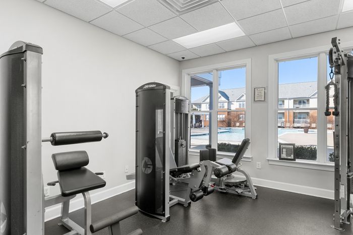 Modern apartment gym with state-of-the-art equipment and large windows overlooking a sparkling outdoor pool.