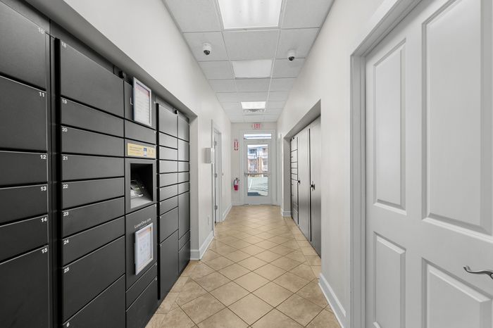Modern apartment corridor featuring secure mailbox lockers and tiled flooring, leading to a bright exit door.