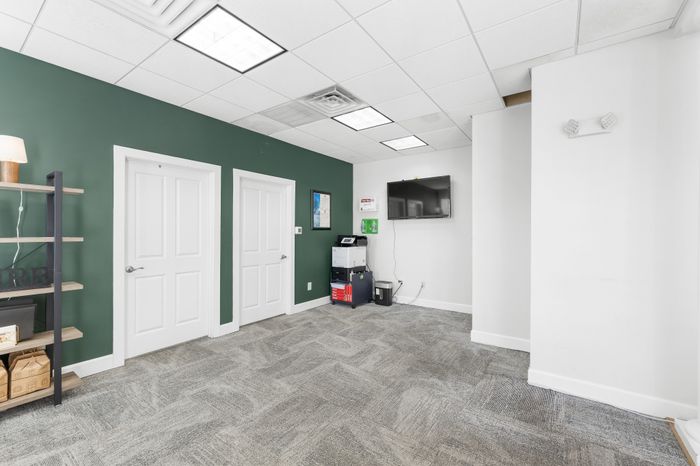 Bright and modern office space featuring a green accent wall, sleek shelving unit, and wall-mounted TV, perfect for professional settings.