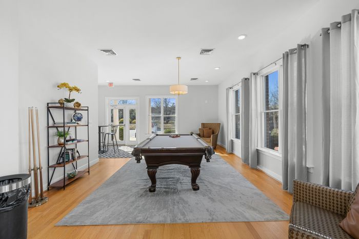 Chic communal lounge featuring a stylish pool table, elegant wooden flooring, and abundant natural light from large windows.