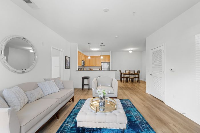 Bright open-plan living area featuring elegant seating, a plush blue rug, modern kitchen, and stylish dining space.