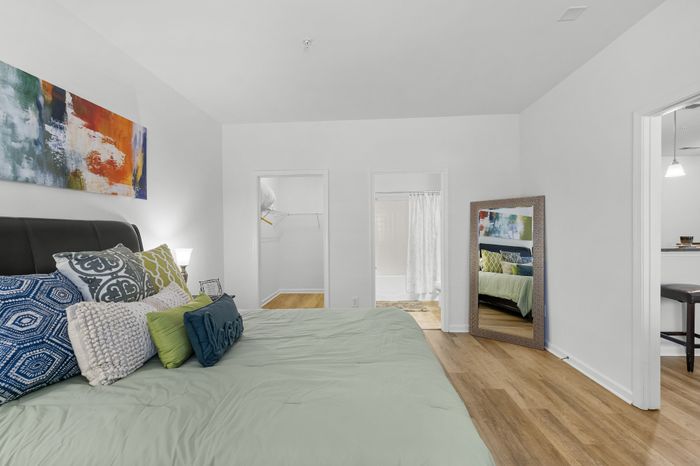 Modern bedroom with elegant decor, featuring a luxurious bed, hardwood floors, and a spacious walk-in closet with an adjacent bathroom.