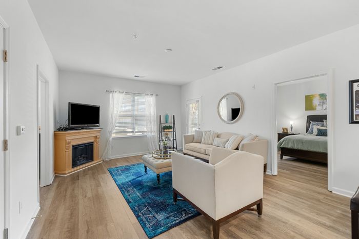 Bright, inviting living room with cozy seating, a decorative fireplace, and natural light from large windows, connecting to a stylish bedroom.