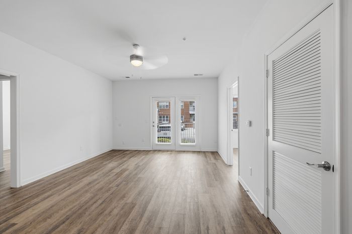 Bright, open-concept living space with sleek hardwood floors, modern ceiling fan, and double glass doors leading to outdoor view.