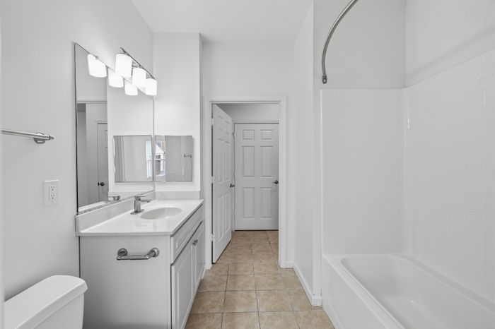 Bright, modern bathroom featuring elegant white fixtures, a sleek vanity with large mirror, and a spacious tub.