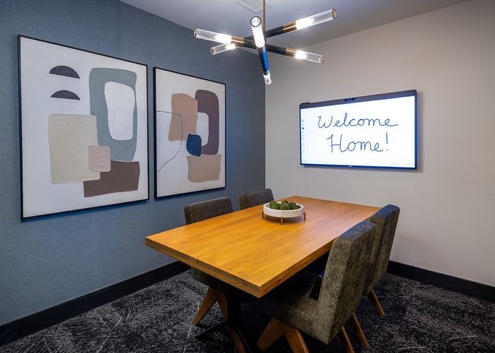 Modern dining room with stylish abstract art and a warm wooden table, accented by a vibrant light fixture and a welcoming digital message.
