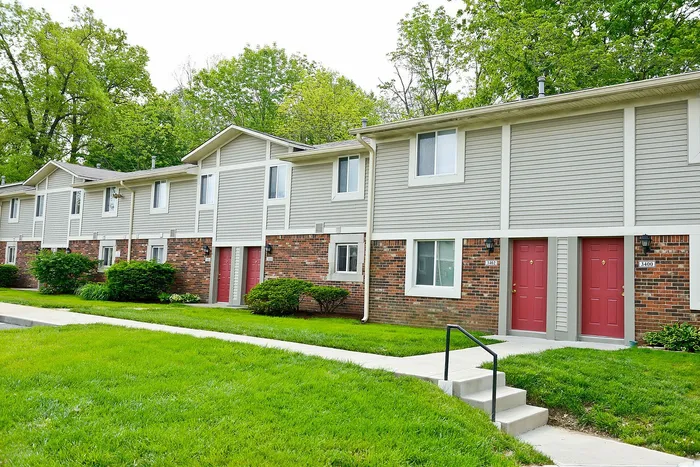 Charming row of townhouses with vibrant red doors and lush landscaping, set against a backdrop of lush green trees.