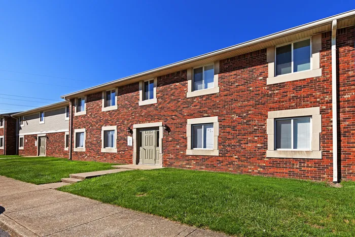 Charming red-brick apartment building with pristine green lawn and sunny blue sky, perfect for comfortable living.
