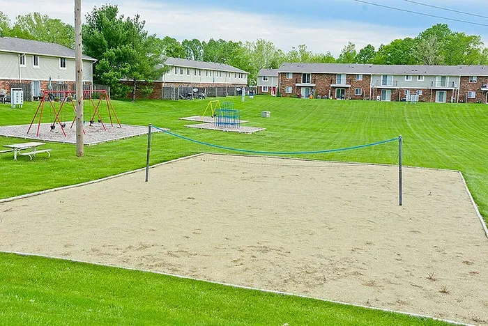 Inviting outdoor community space featuring a sand volleyball court, lush green lawns, and a vibrant playground in a serene apartment complex setting.