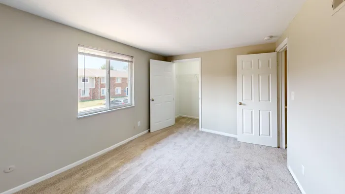 Inviting bedroom with plush carpeting, bright window view, and spacious closet offering a blend of comfort and style.