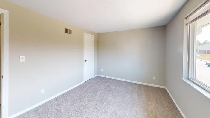 Bright, spacious room with soft carpet, neutral walls, and a large window offering natural light.