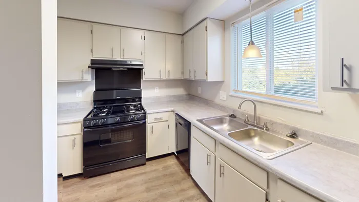 Contemporary kitchen featuring sleek white cabinets, modern black appliances, and ample natural light from a large window.