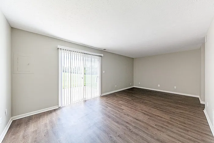 Bright and spacious living area with modern wood flooring and large sliding glass door leading to a lush, green outdoor view.