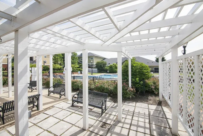 Charming outdoor patio with elegant white pergola, stylish seating, lush garden, and inviting pool view.