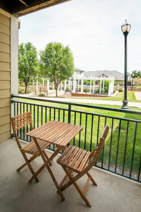 Charming balcony view featuring a cozy wooden table set, lush green grass, and scenic outdoor pergola area perfect for relaxation.