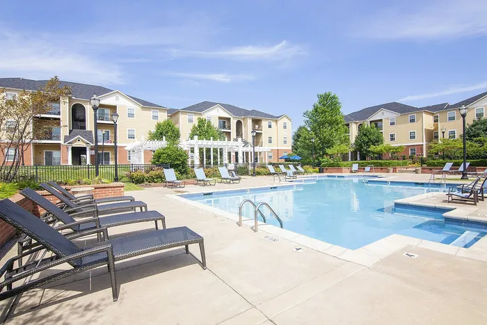 Inviting residential complex showcasing a sparkling outdoor pool, surrounded by elegant lounging chairs and vibrant landscaping, under a clear blue sky.